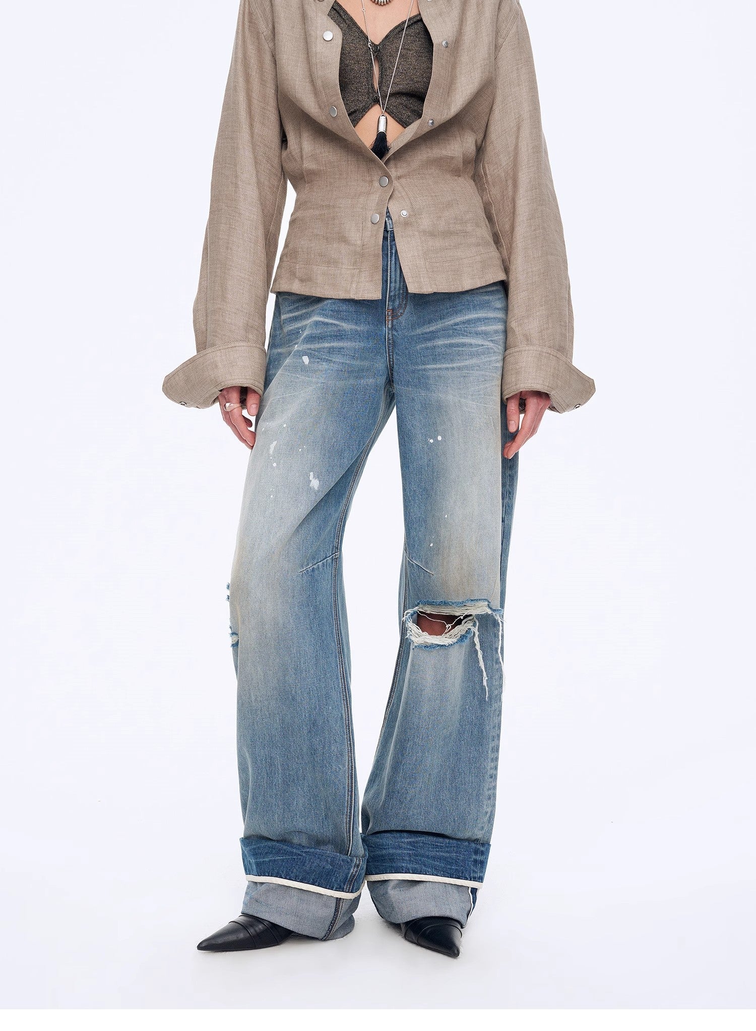 Person wearing a beige jacket and ripped blue jeans on a white background
