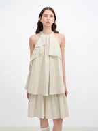 Woman wearing a beige halter neck dress with layered design on a white background