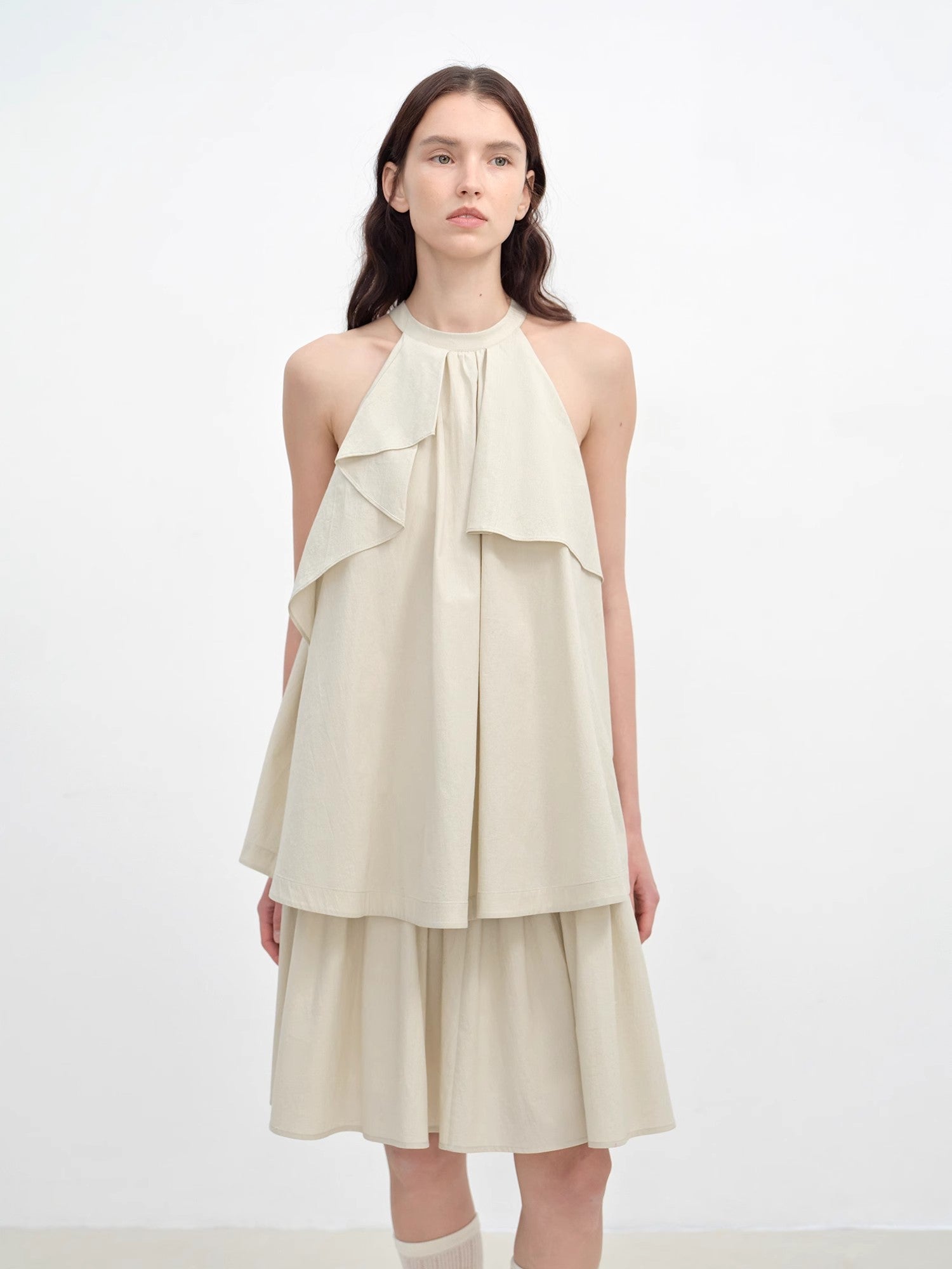 Woman wearing a beige halter neck dress with layered design on a white background