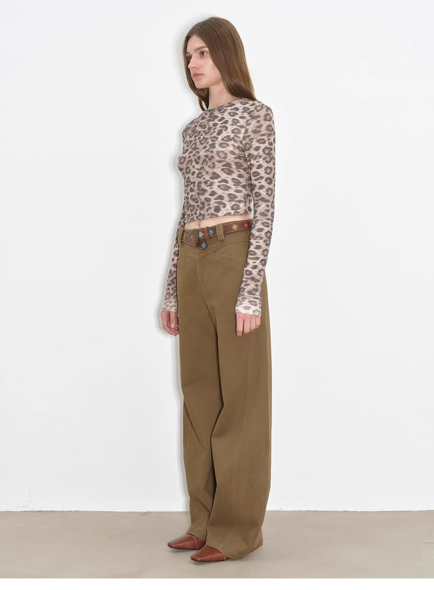 Woman wearing a leopard print top and brown pants against a white background