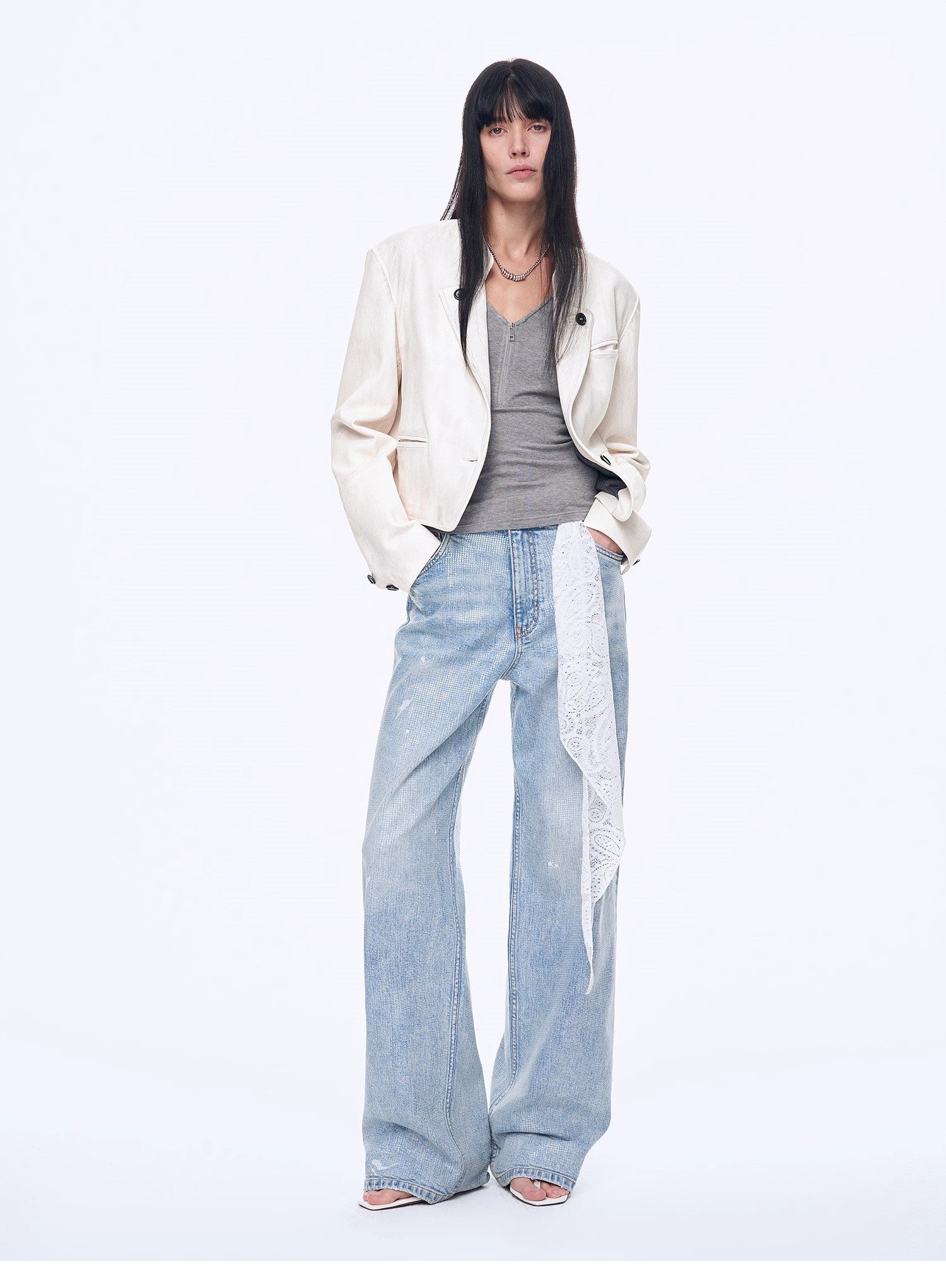 Person wearing a white blazer, gray top, and light blue jeans on a white background