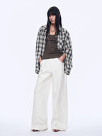 Person wearing a plaid shirt, brown top, and white pants on a white background
