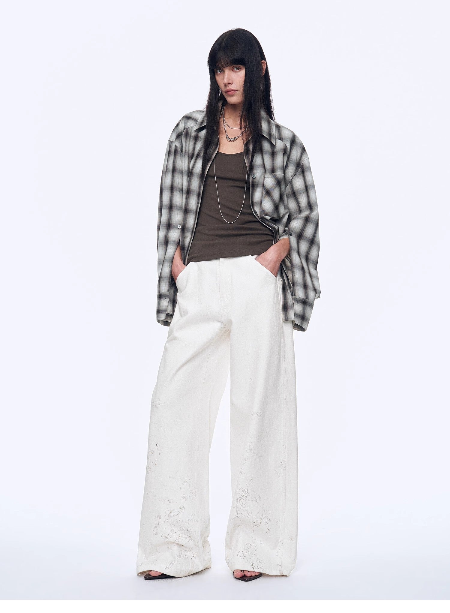 Person wearing a plaid shirt, brown top, and white pants on a white background