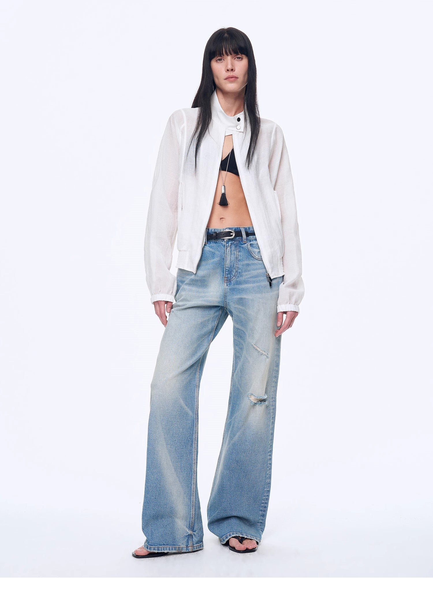 Woman wearing a white shirt, black bra, and light blue jeans on a white background
