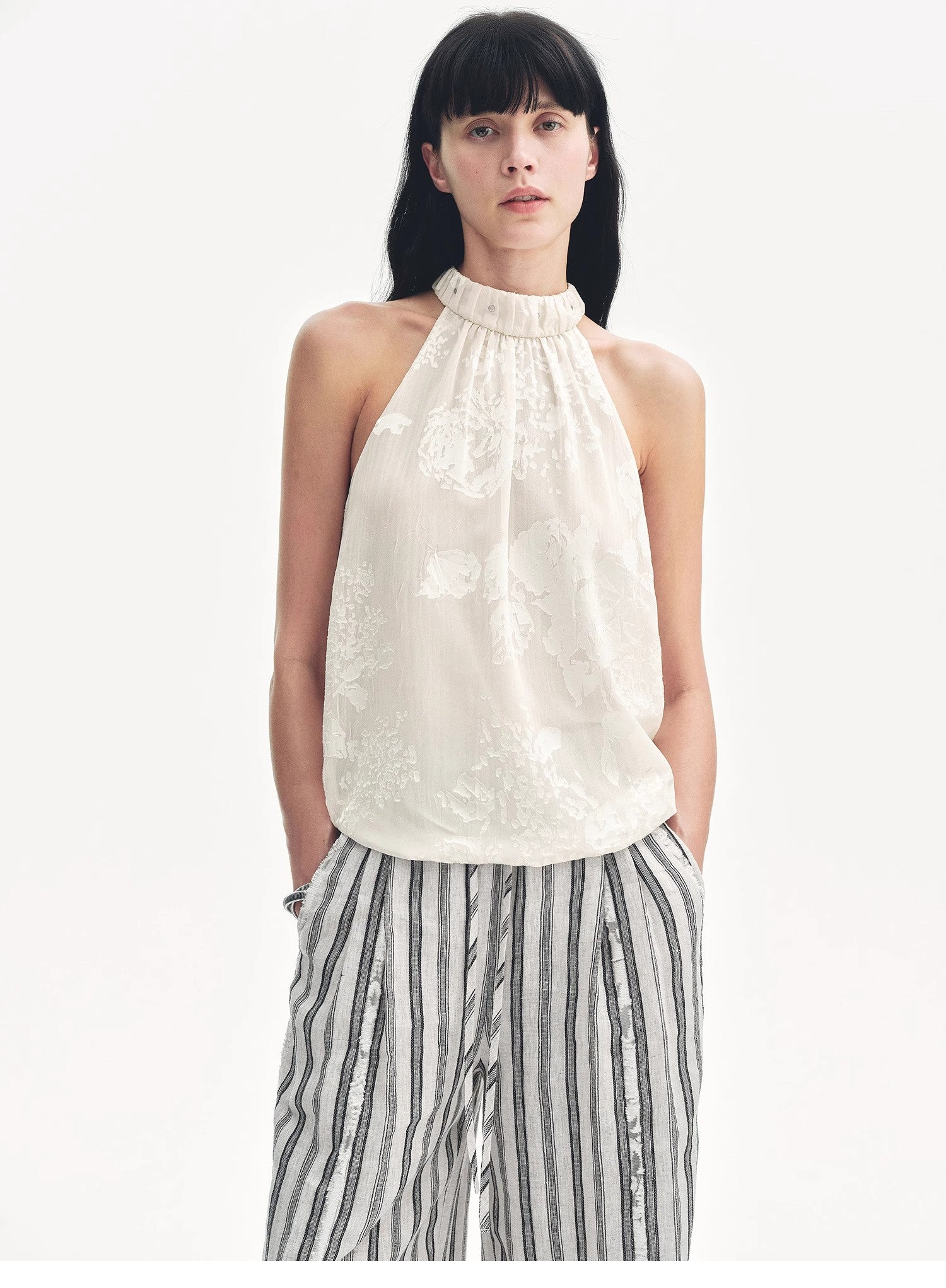 Woman wearing a white sleeveless top and striped pants on a white background