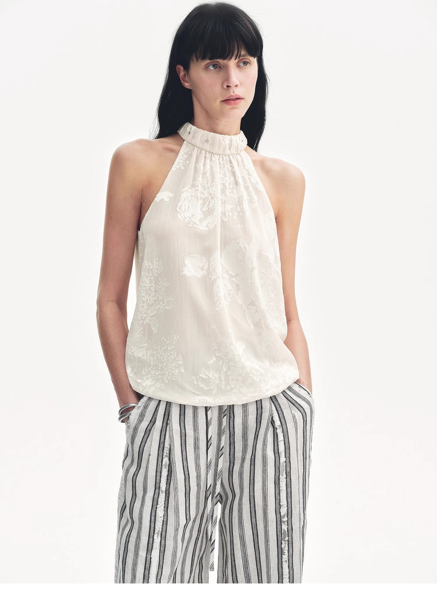 Woman wearing a white sleeveless top and striped pants on a white background