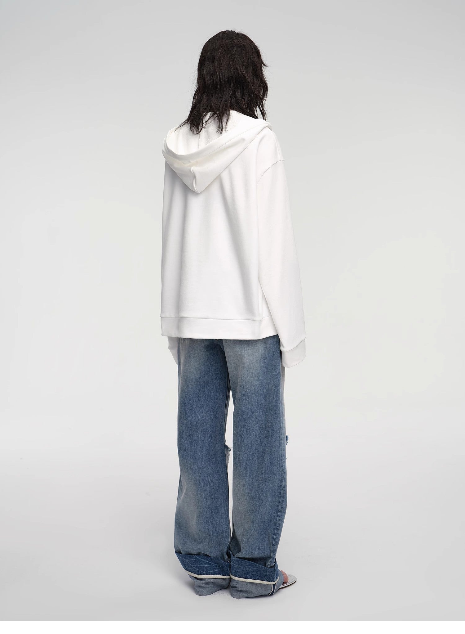 Person wearing a white hoodie and blue jeans on a plain background