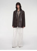 Person wearing a dark leather jacket and white pants on a white background