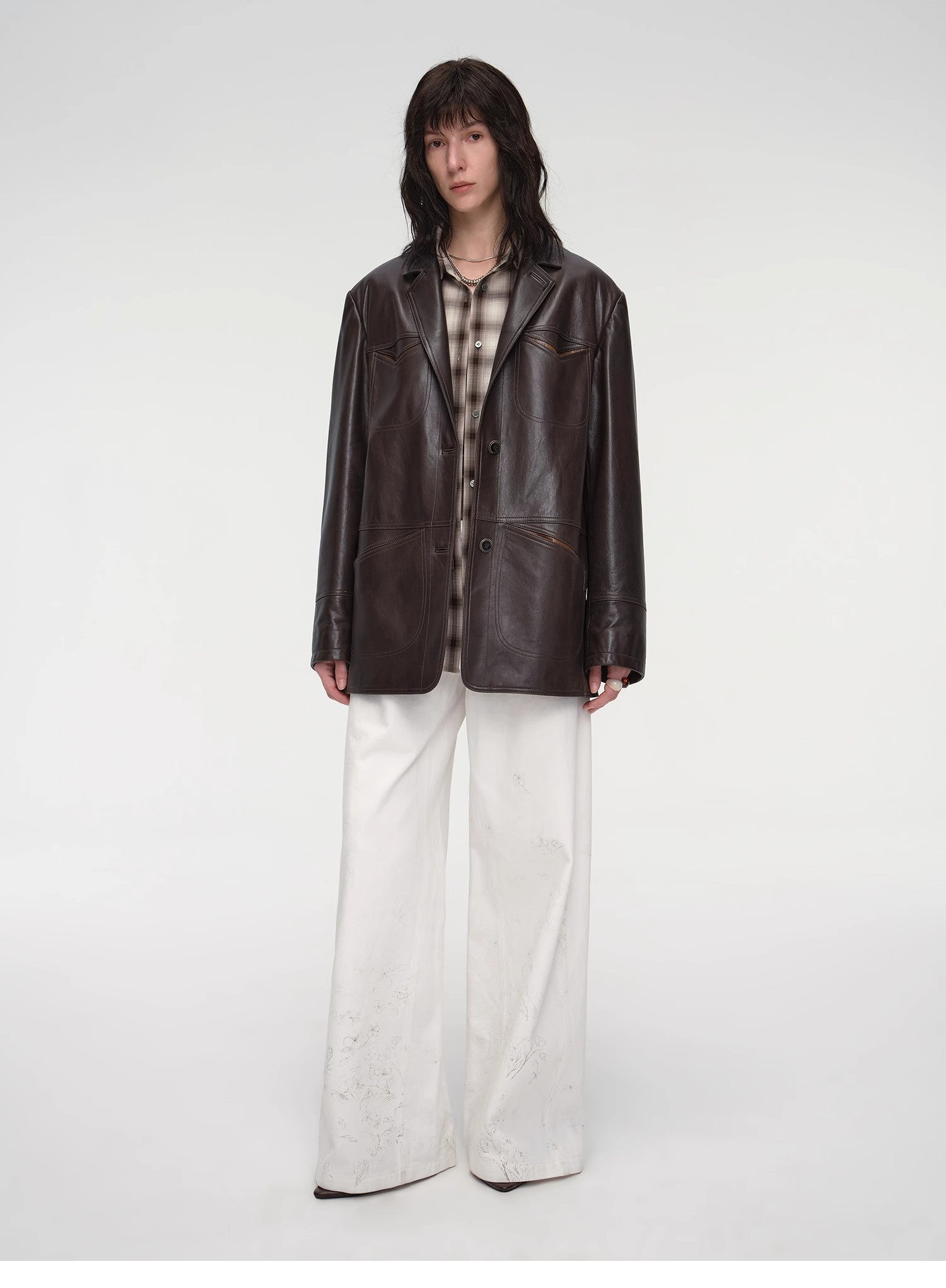 Person wearing a dark leather jacket and white pants on a white background