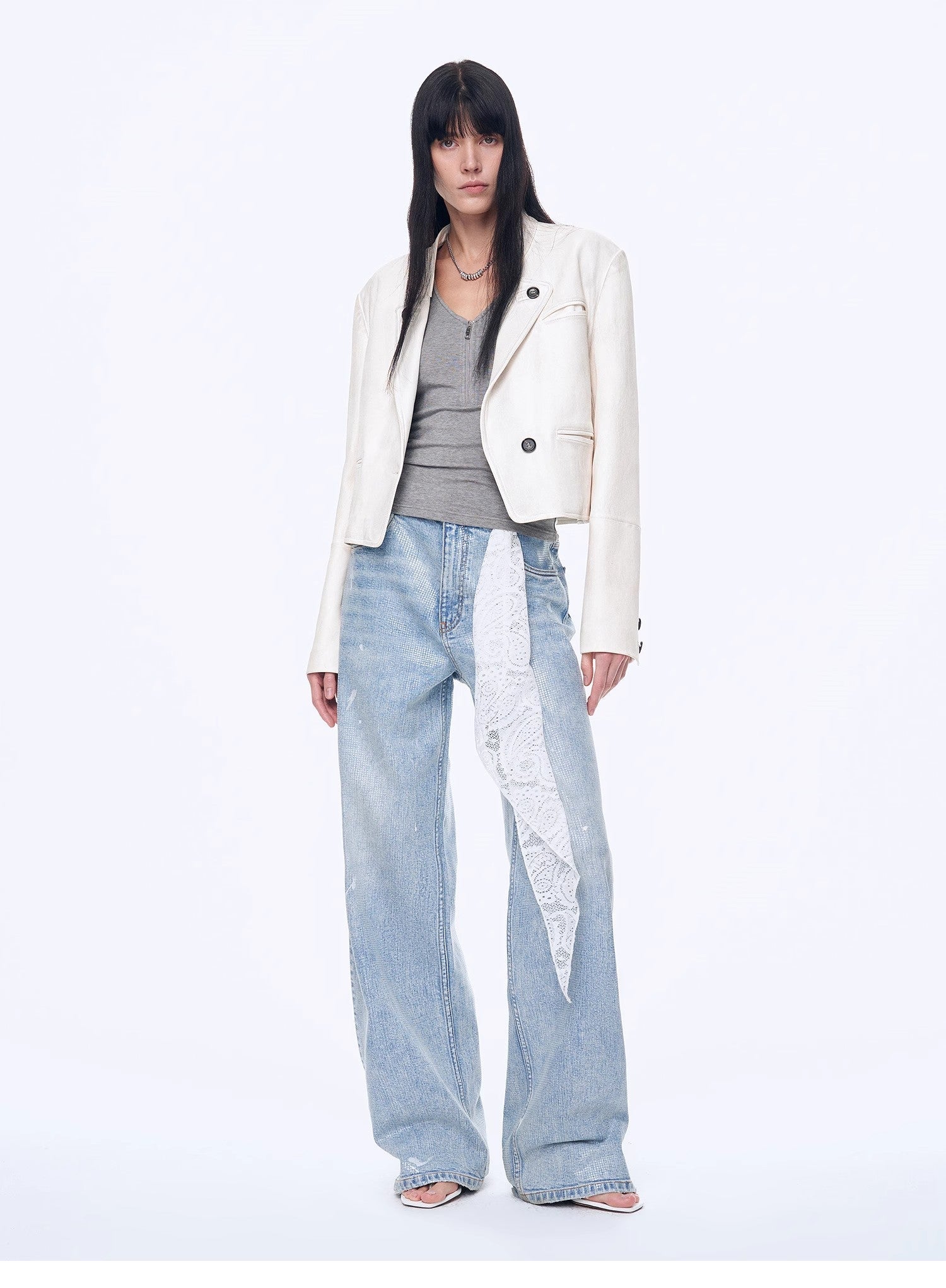 Person wearing a white blazer, gray top, and light blue jeans on a white background