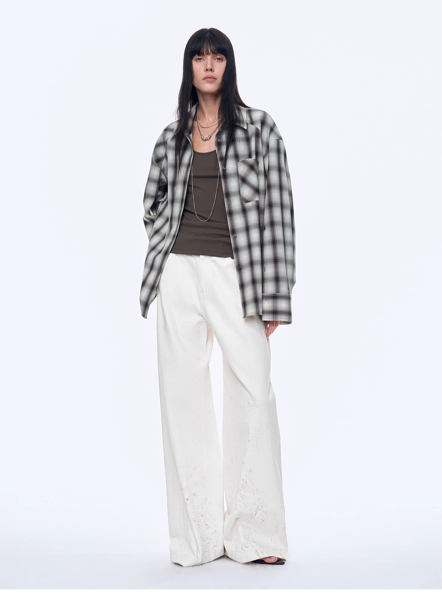 Person wearing a plaid shirt, brown top, and white pants on a white background