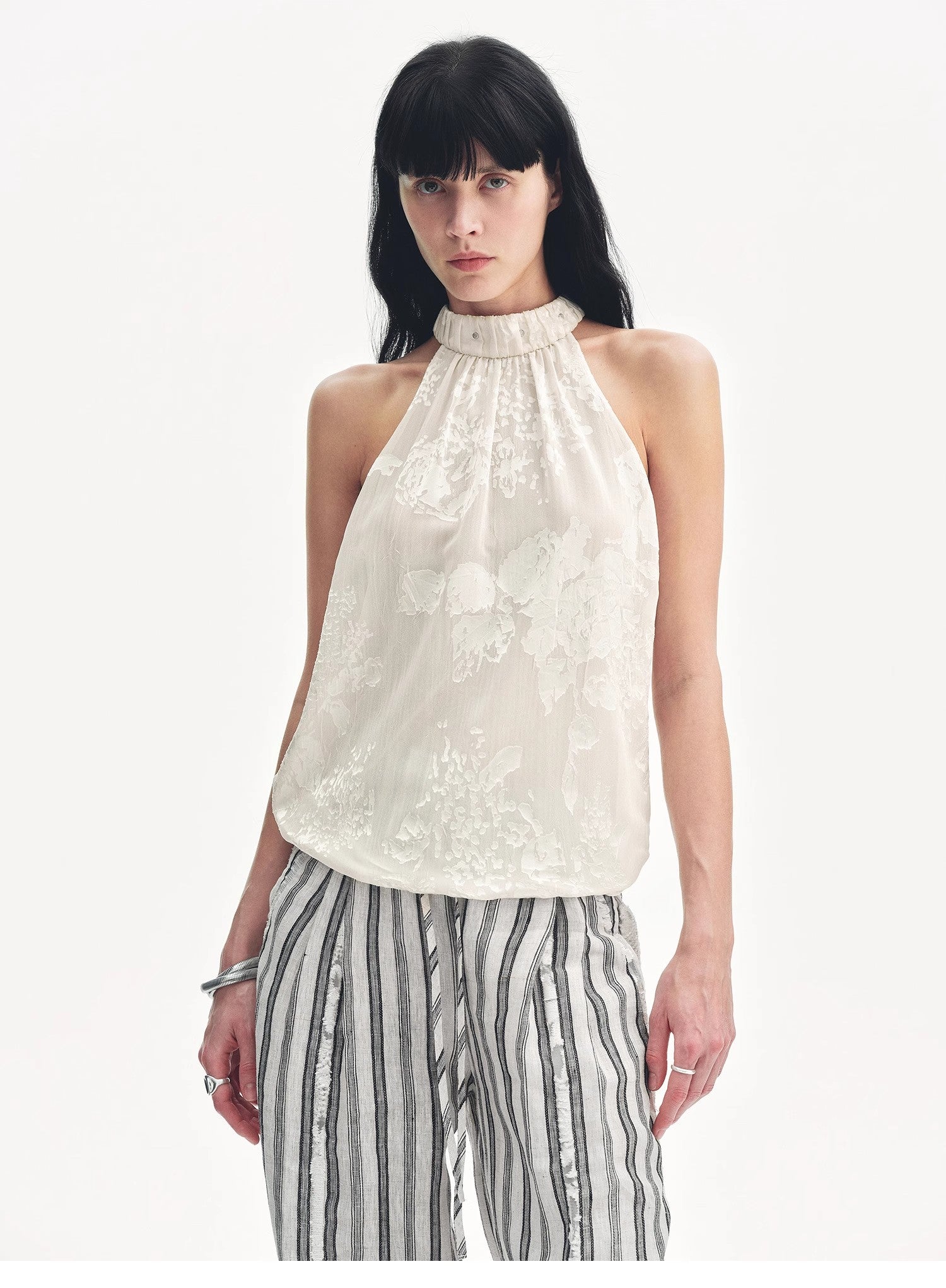 Woman wearing a white sleeveless top with a high neckline and striped pants on a white background