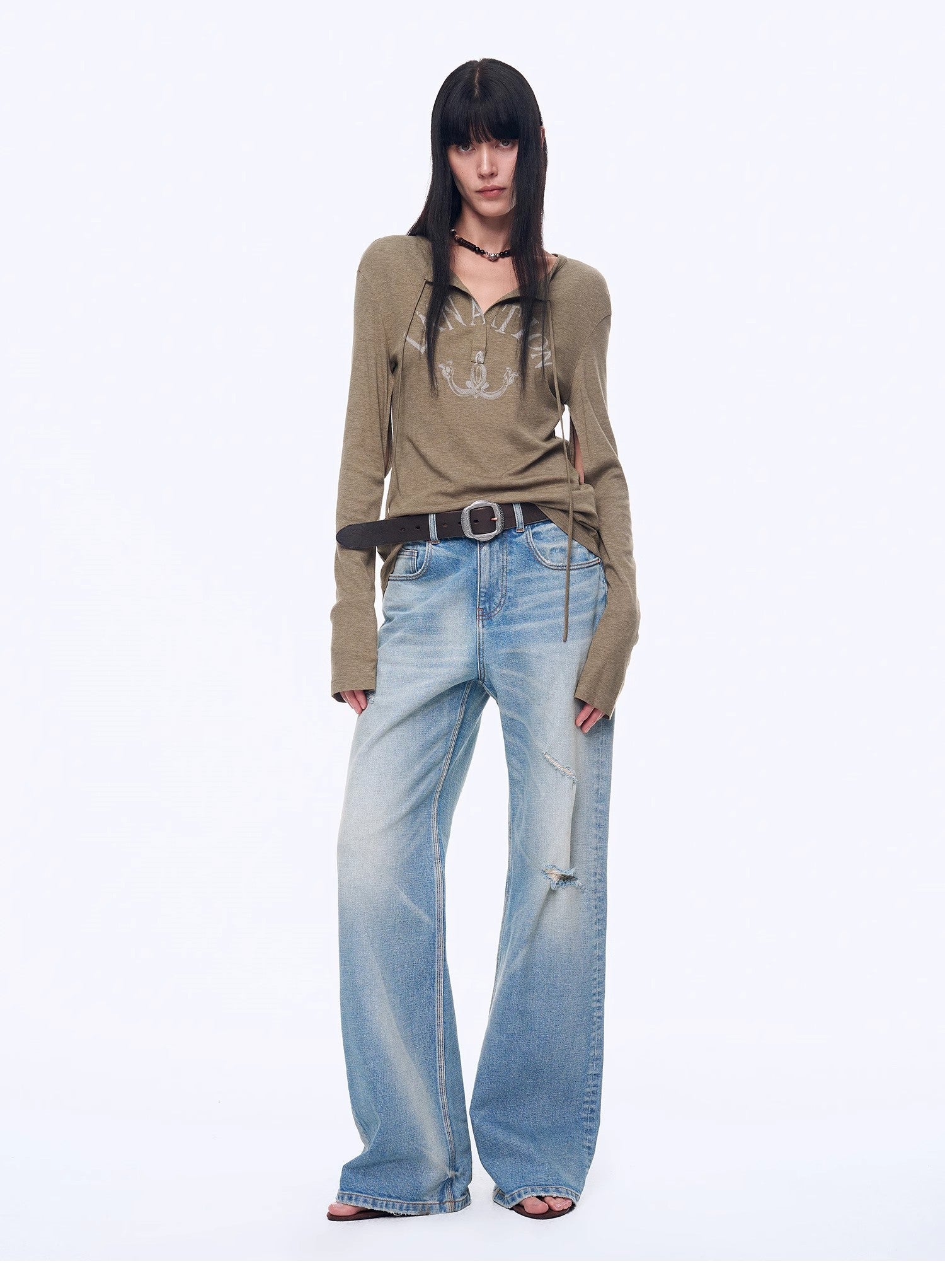 Woman wearing a beige long-sleeve top and blue jeans on a white background