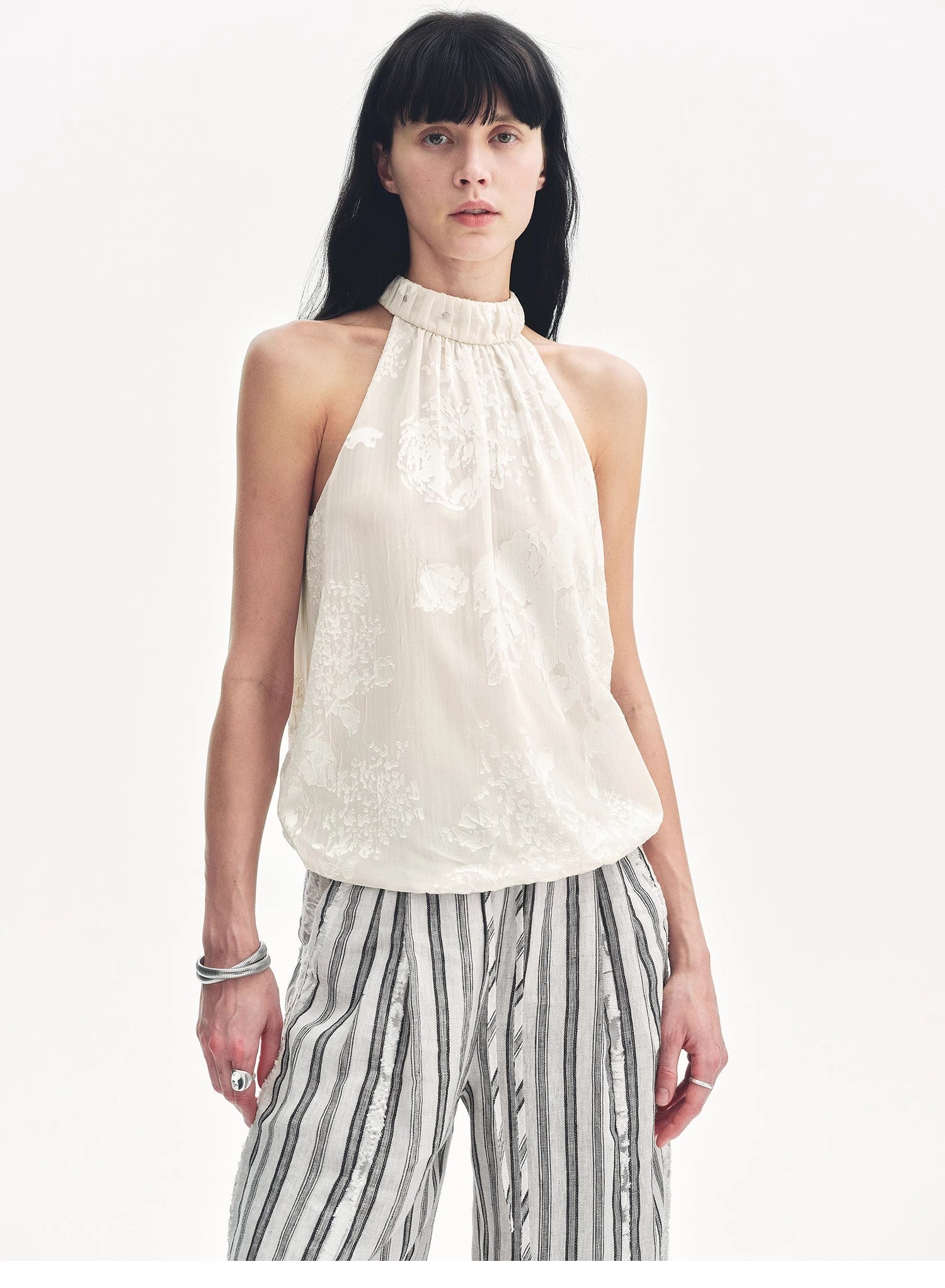 Woman wearing a white sleeveless top and striped pants on a white background