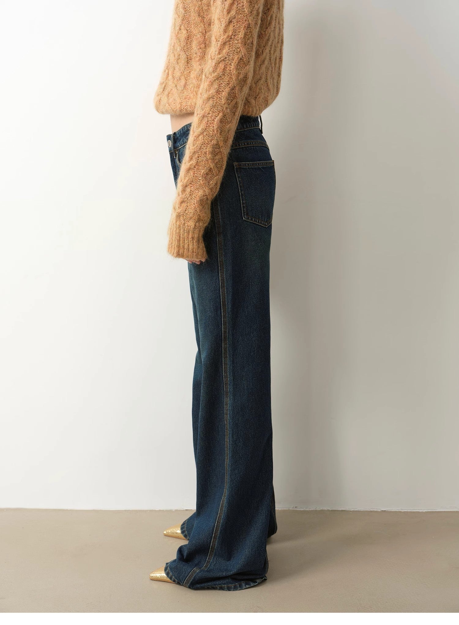 Person wearing a beige sweater and dark blue jeans against a plain background