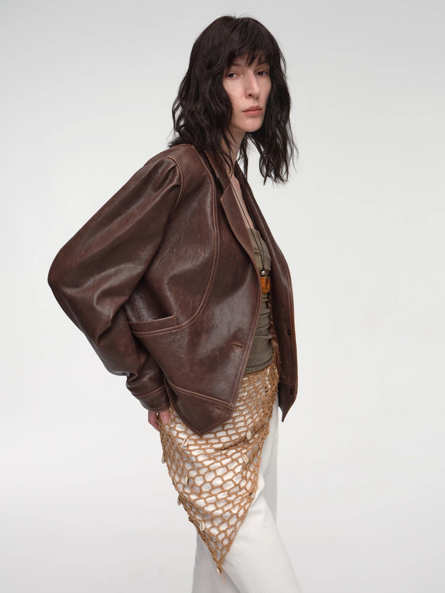Person wearing a brown leather jacket and a textured beige skirt on a white background