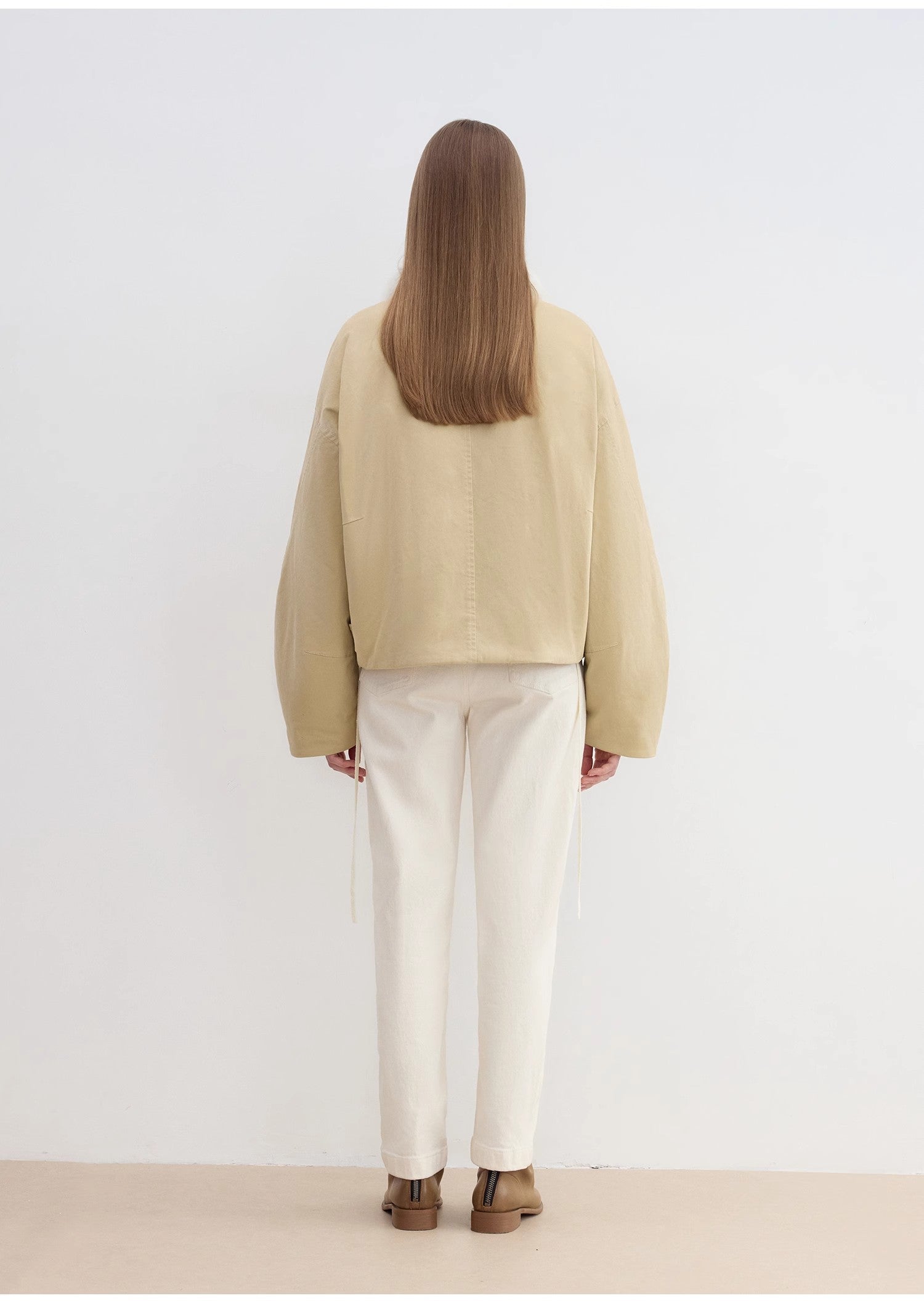 Person wearing a beige jacket and white pants on a plain background