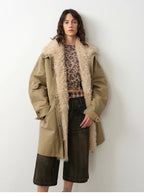 Woman wearing a long beige coat with fur trim against a white background