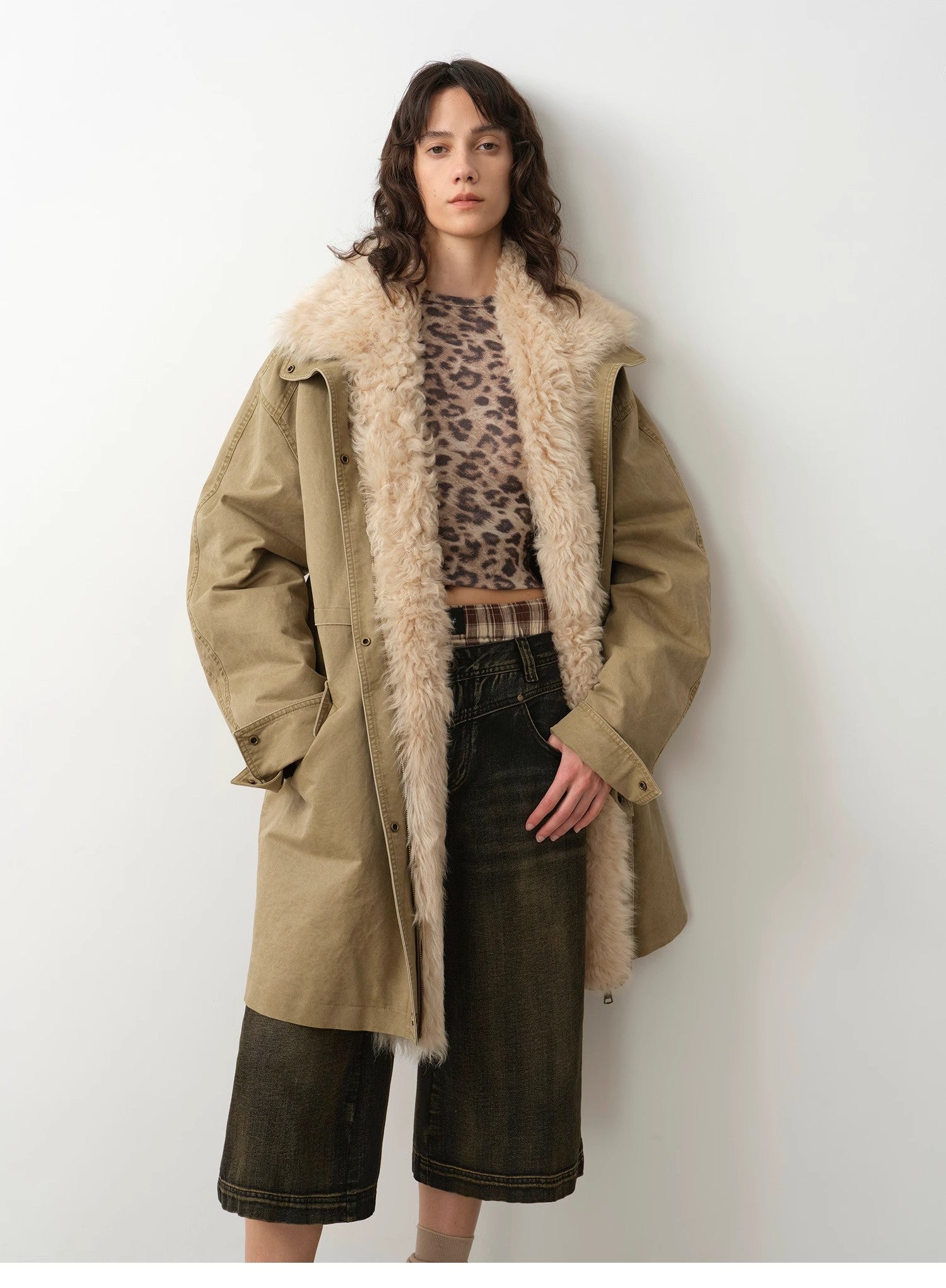 Woman wearing a long beige coat with fur trim against a white background