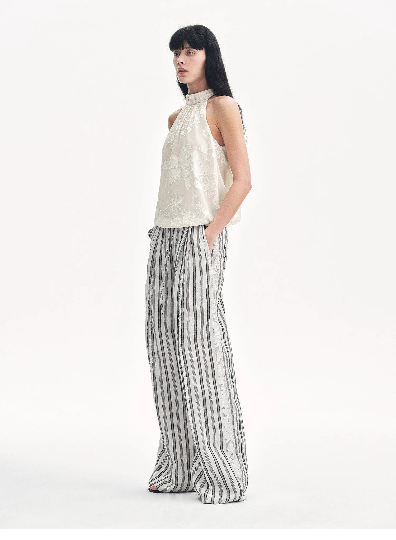 Woman wearing a sleeveless top and striped pants on a white background