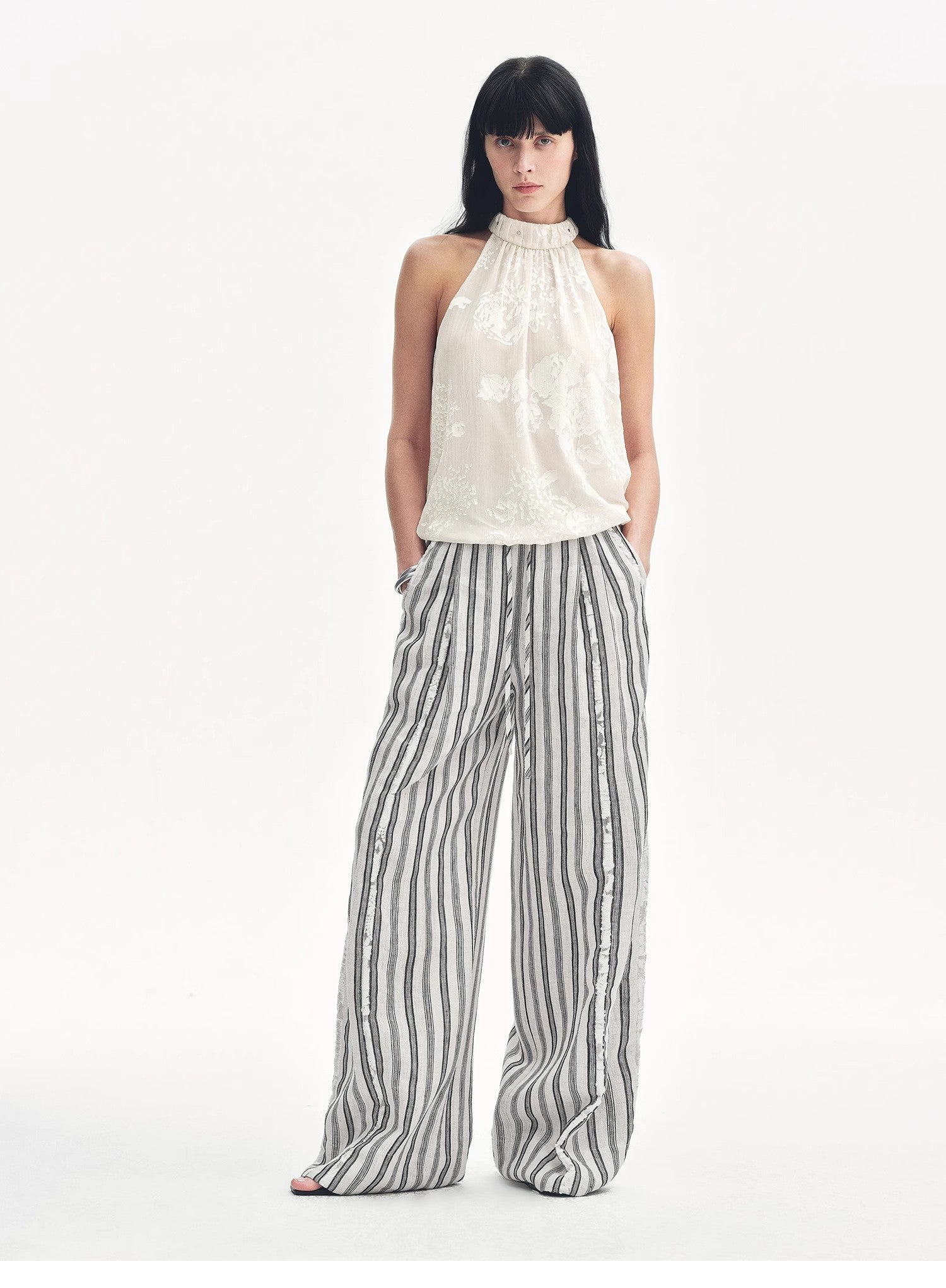 Woman wearing a white halter top and striped pants on a white background