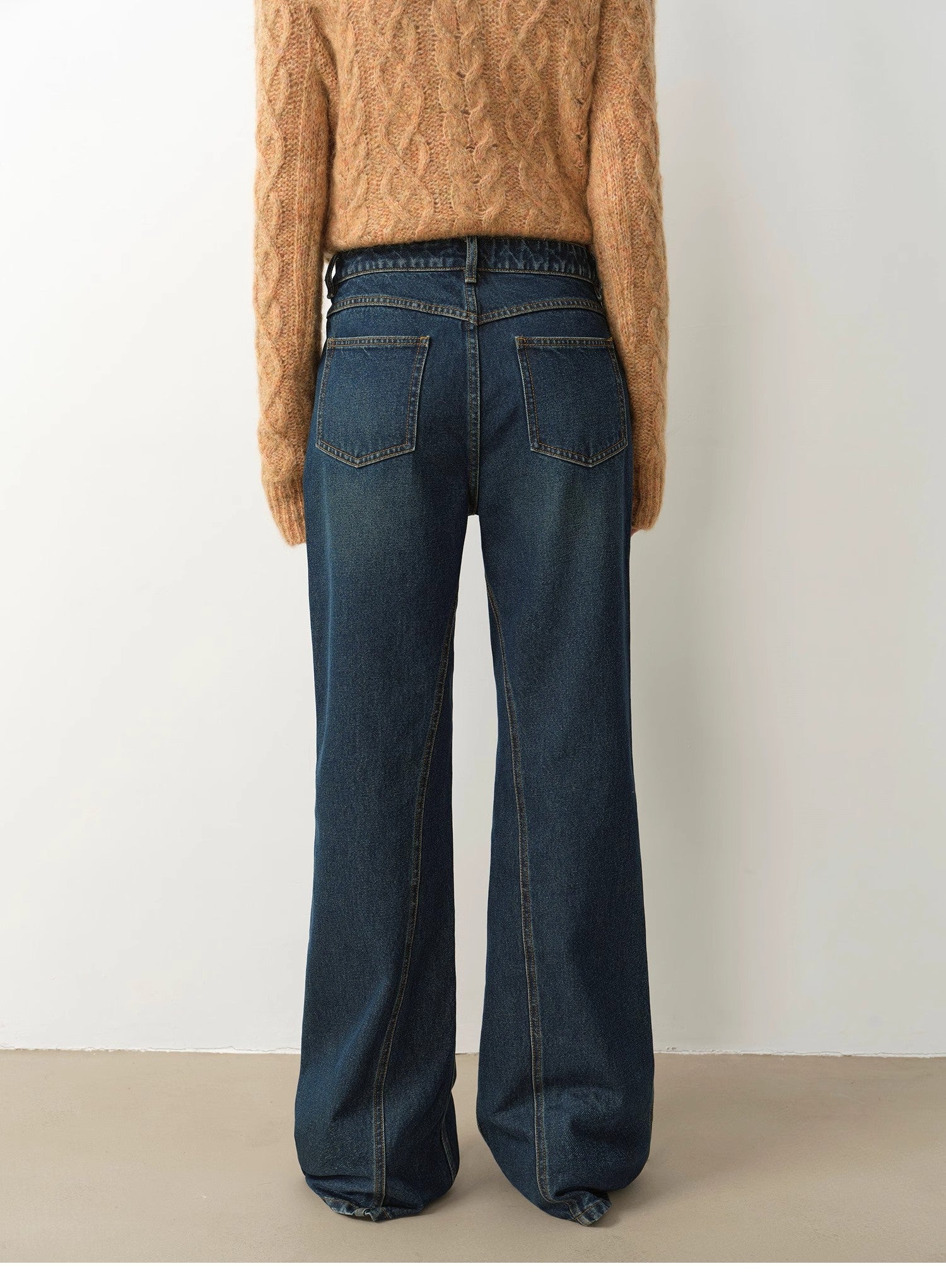 Person wearing blue flared jeans and a brown sweater against a white background