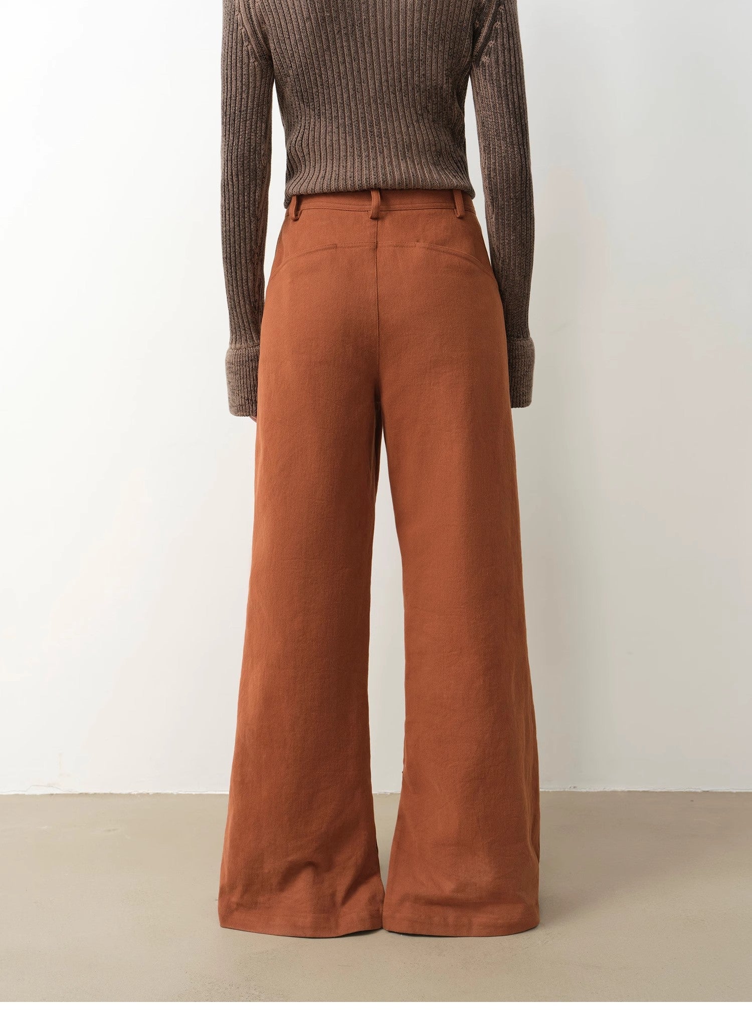 Person wearing a ribbed sweater and brown wide-leg pants on a plain background