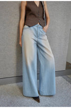Person wearing a brown vest and light blue jeans against a gray wall.