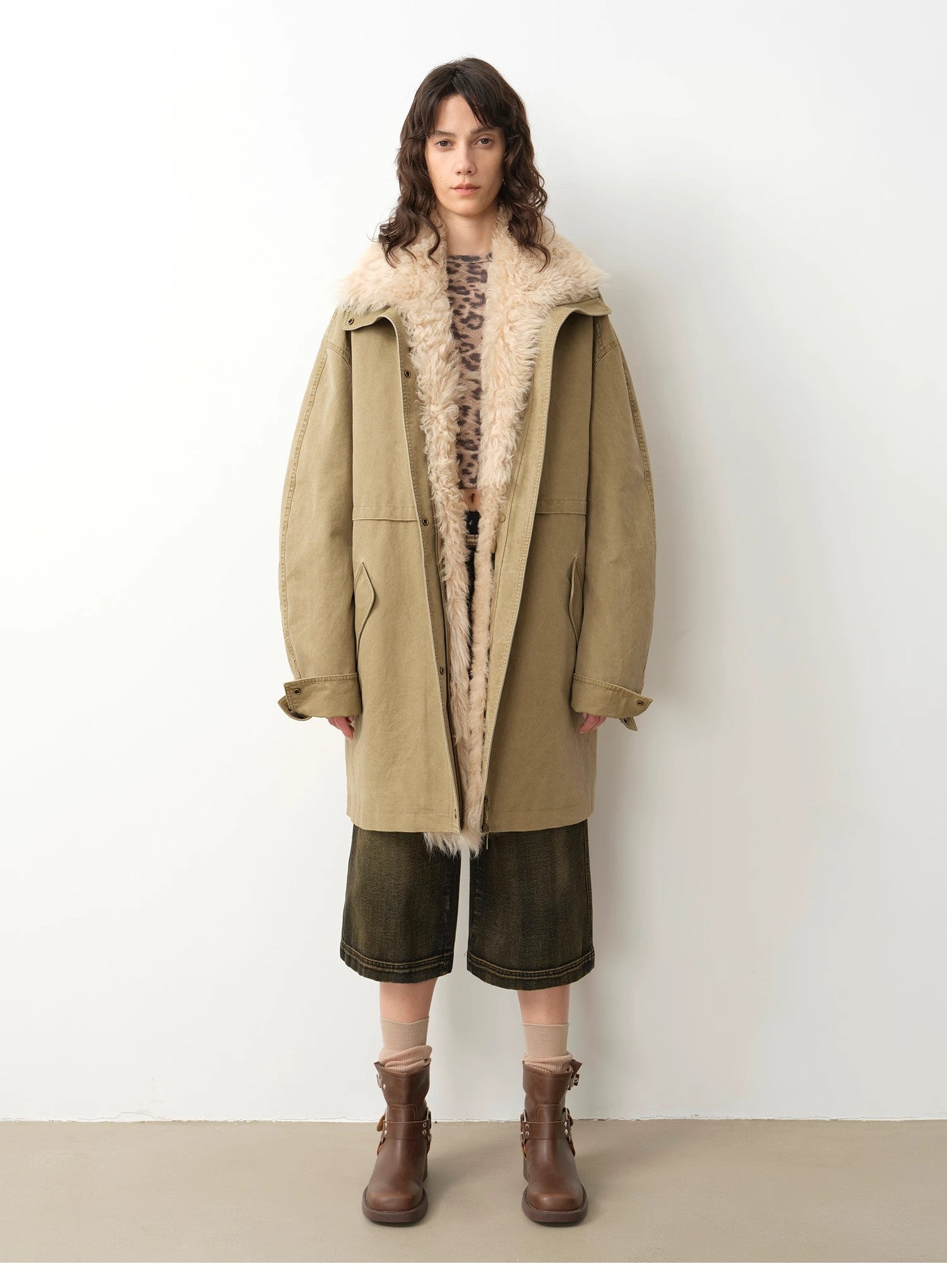 Person wearing a long beige coat with fur lining against a white background