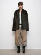 Person wearing a dark fur coat, light shirt, beige pants, and black boots against a white background