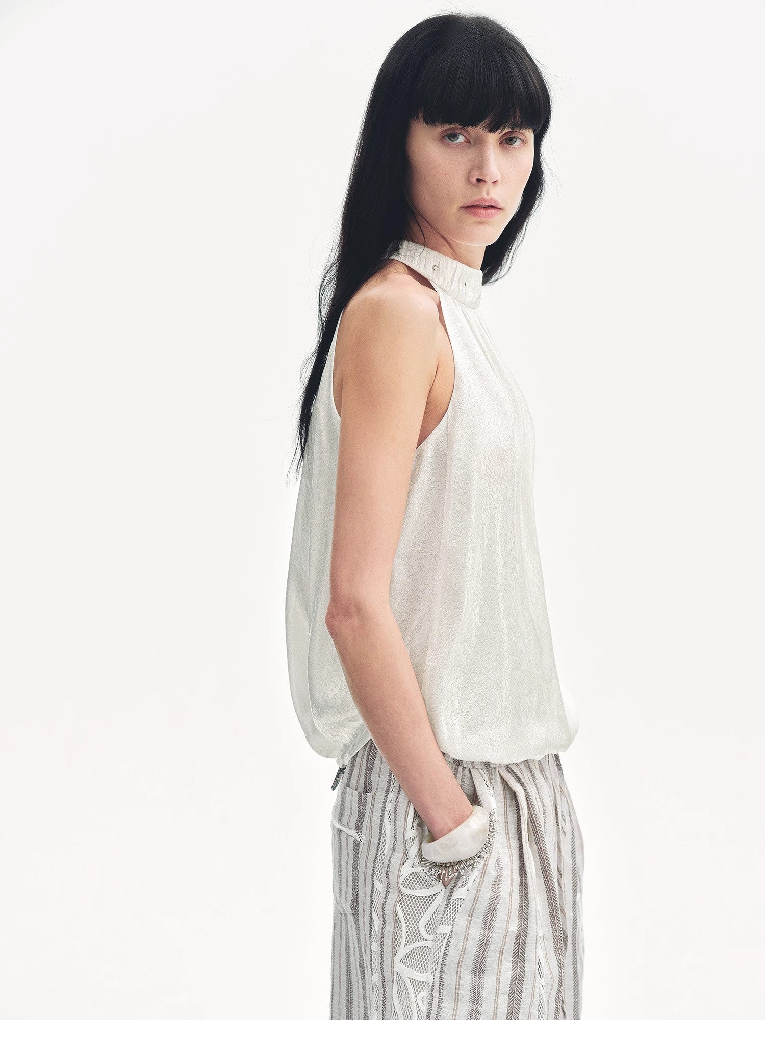 Woman wearing a white sleeveless top and striped pants on a white background