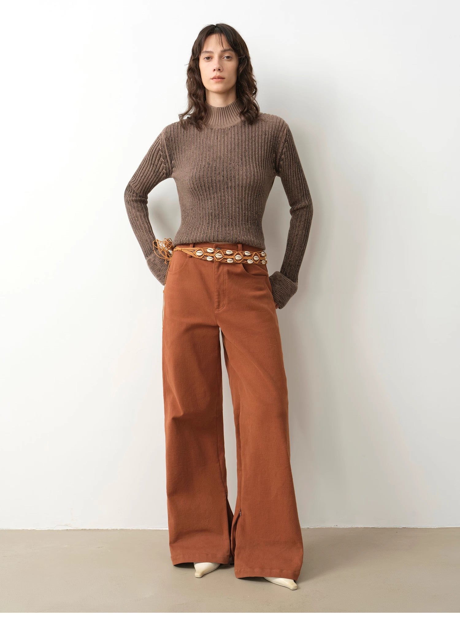 Woman wearing a brown sweater and rust-colored wide-leg pants against a white background