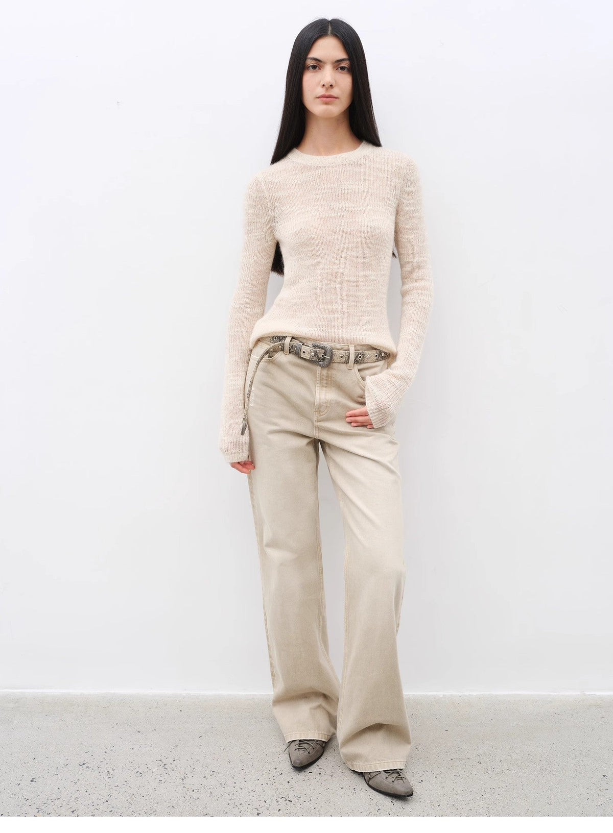 Woman wearing a beige sweater and pants against a white background