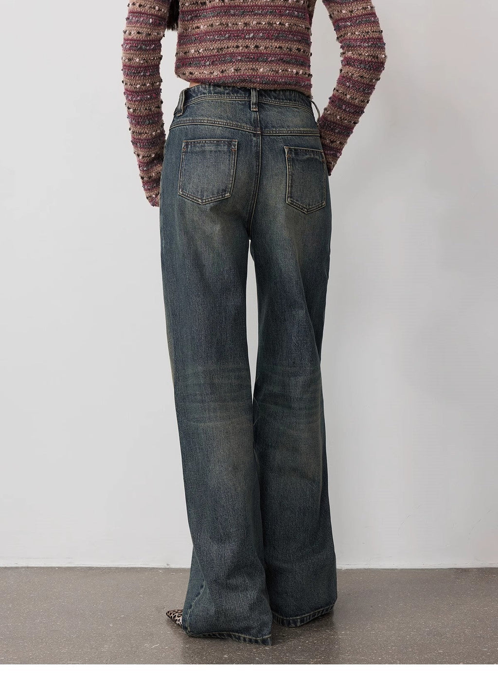Person wearing a patterned sweater and wide-leg jeans against a plain background