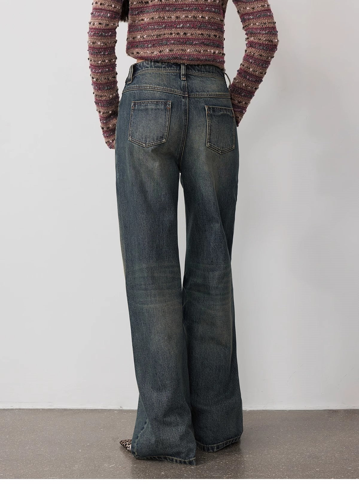 Person wearing a patterned sweater and wide-leg jeans against a plain background