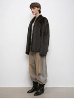 Person wearing a dark fur coat, light pants, and black boots against a white background