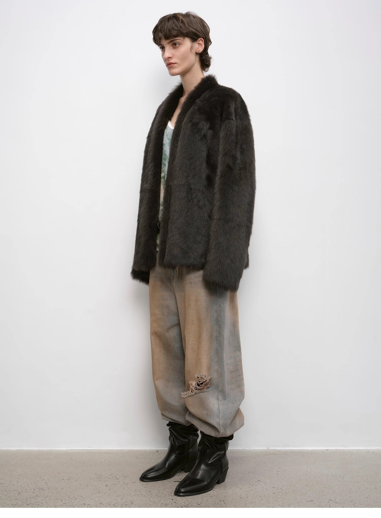 Person wearing a dark fur coat, light pants, and black boots against a white background