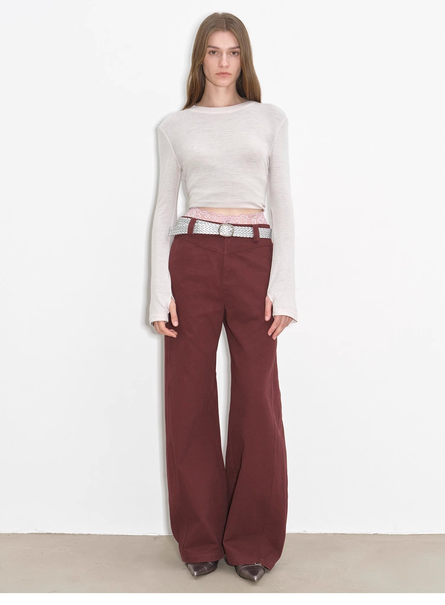 Model wearing a white long-sleeve top and maroon pants on a plain background