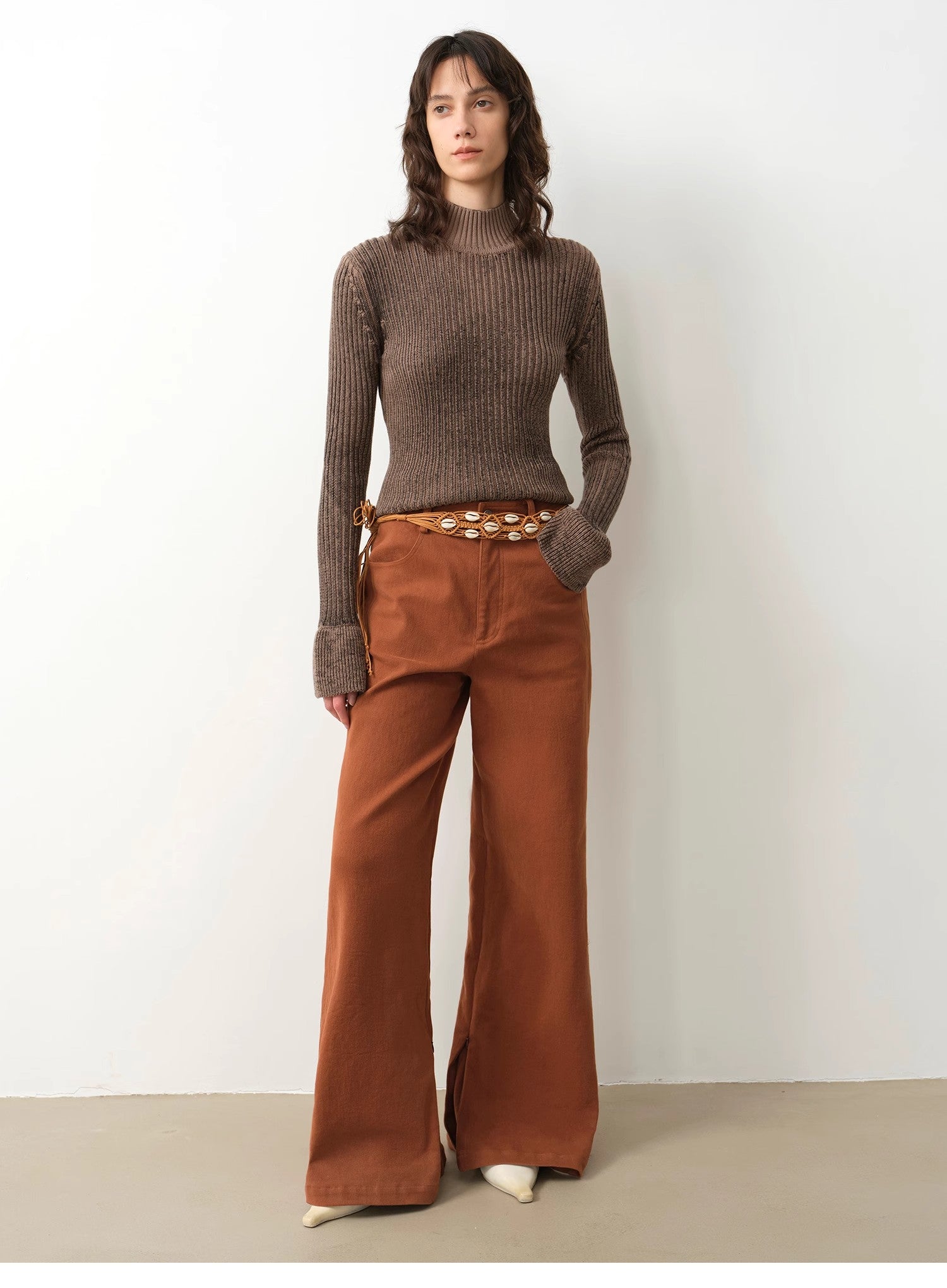 Woman wearing a brown ribbed sweater and rust-colored wide-leg pants against a white background
