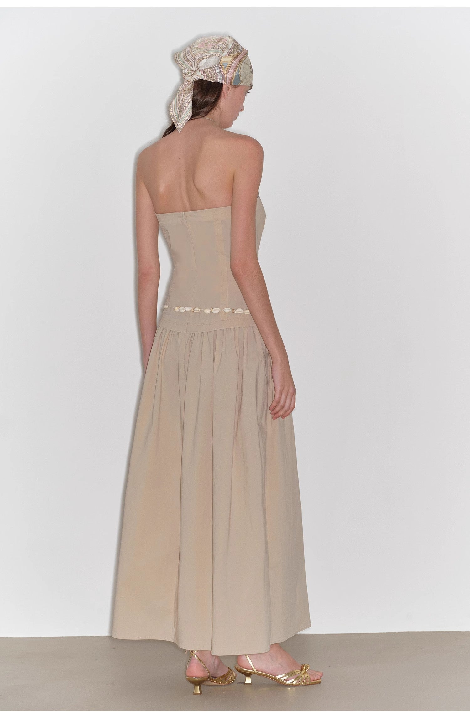 Woman wearing a beige strapless dress with a white background