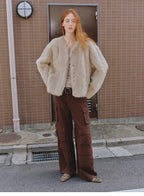 Person wearing a beige fur coat and brown pants standing on a street.