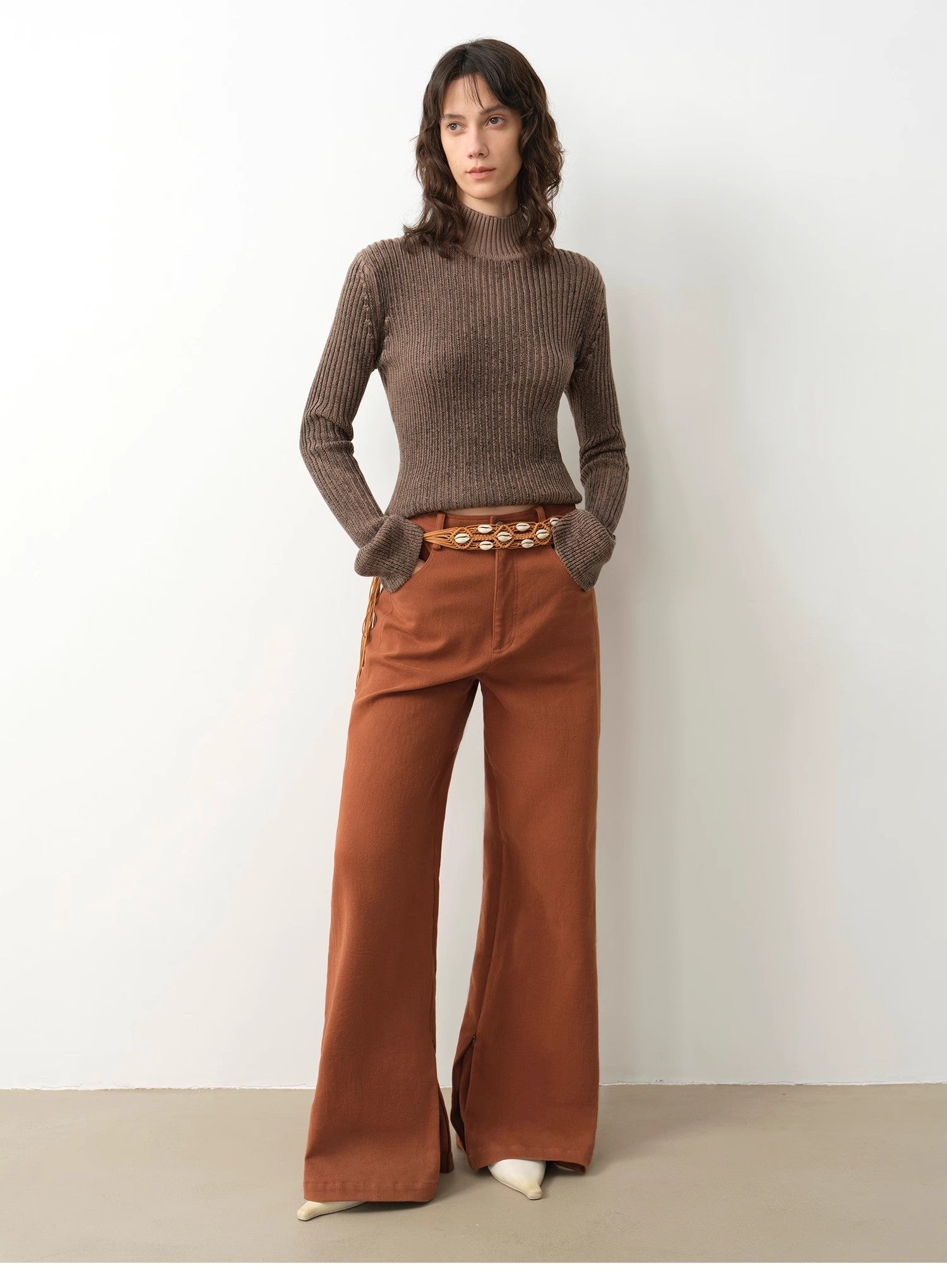 Woman wearing a brown ribbed sweater and rust-colored wide-leg pants against a white background