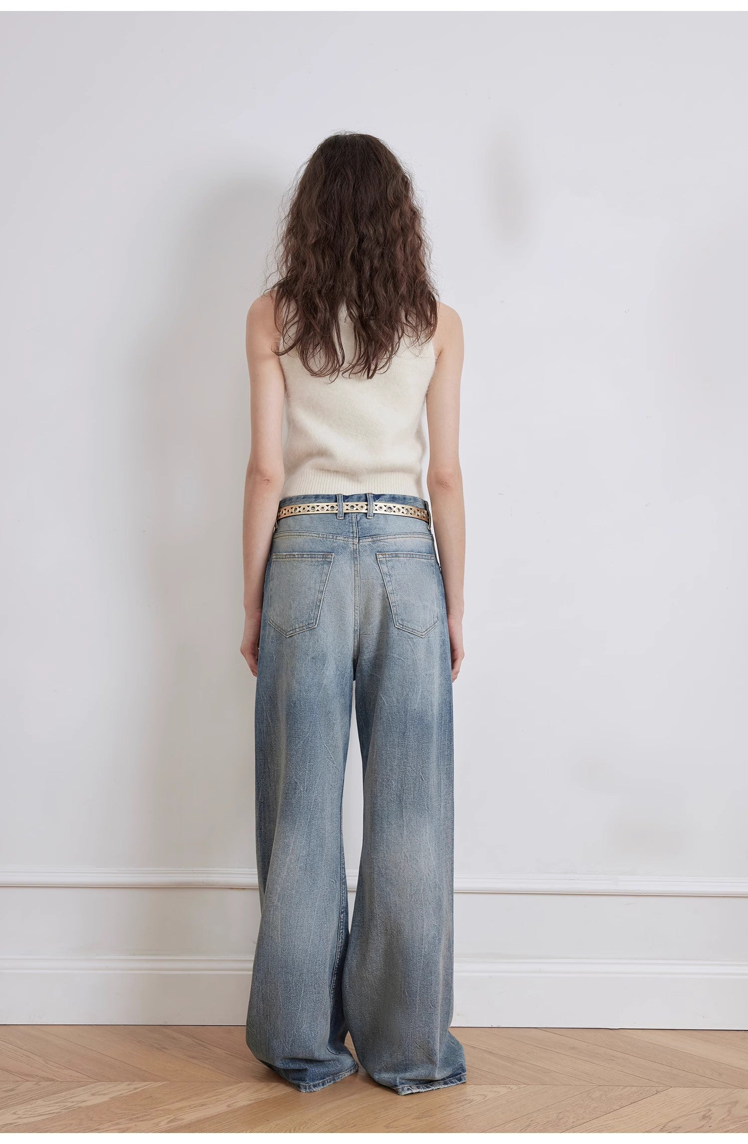 Person wearing a sleeveless top and wide-leg jeans standing against a plain white wall.