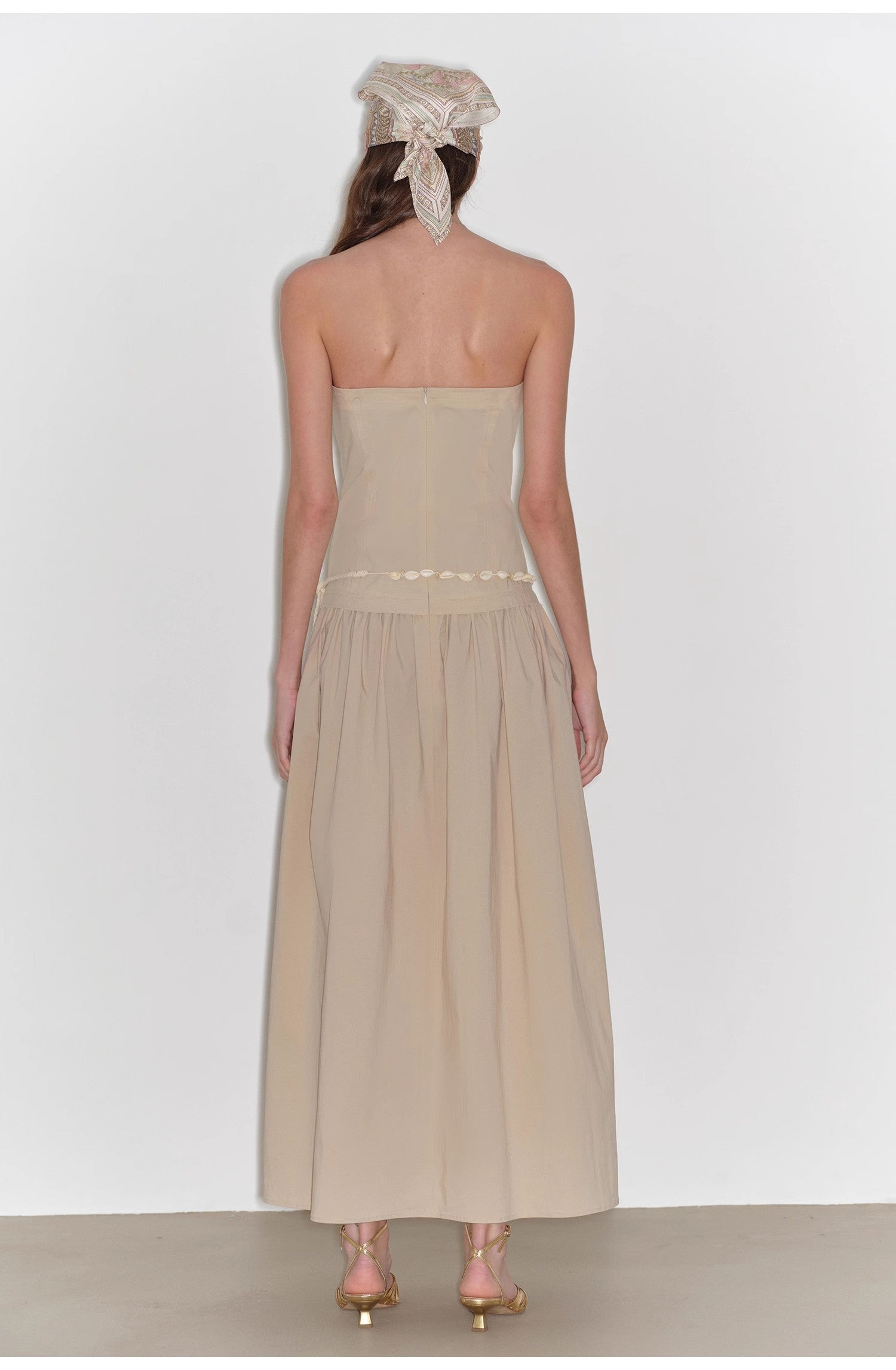 Woman wearing a strapless beige dress with a plain background