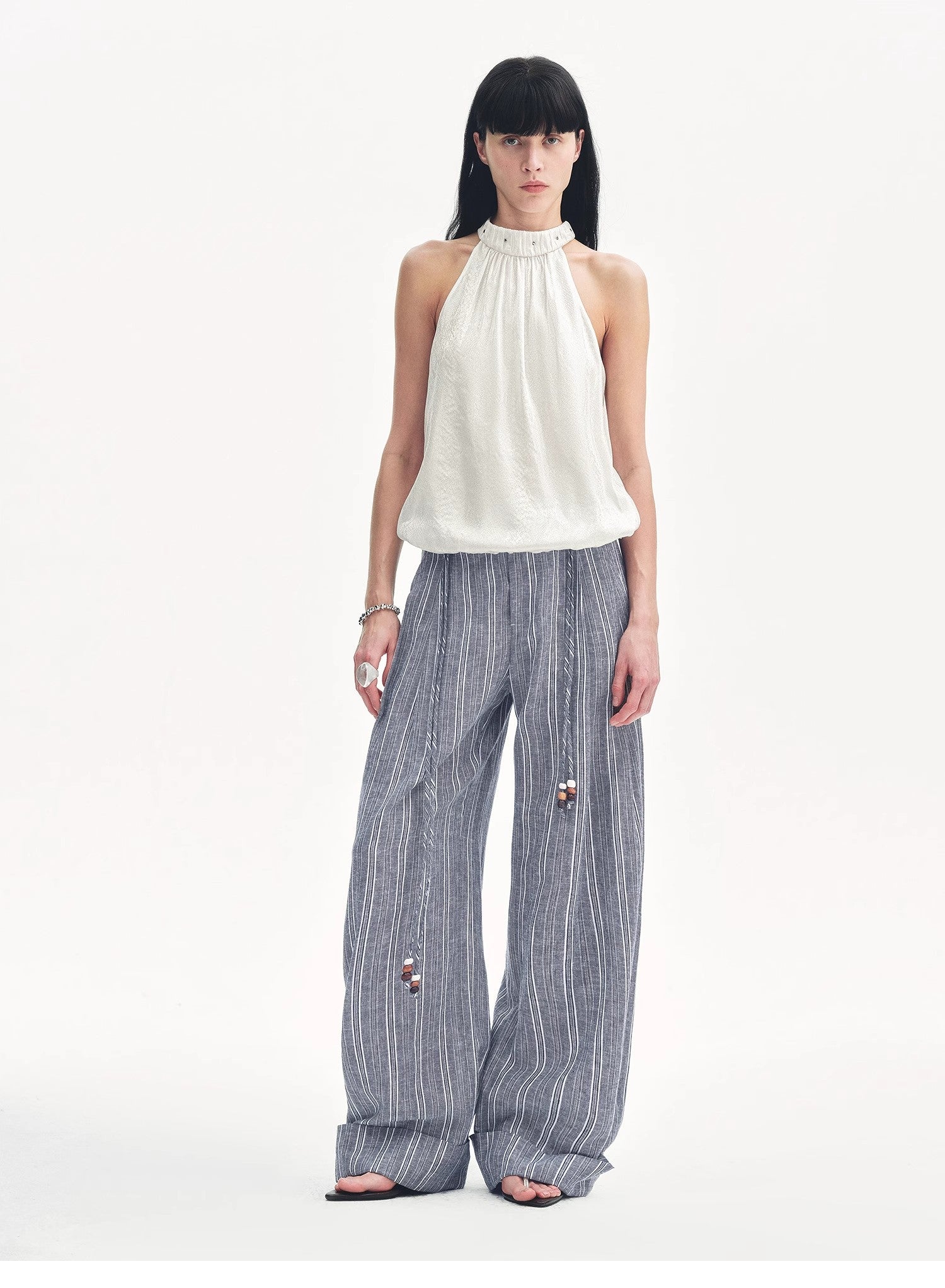 Woman wearing a white sleeveless top and striped pants on a white background