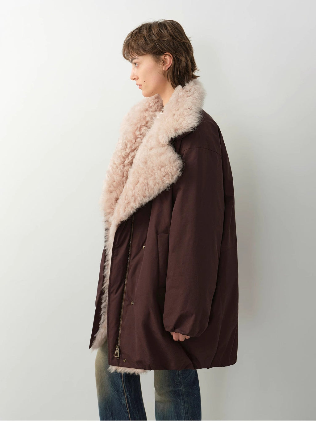 Person wearing a brown coat with beige fur collar against a white background