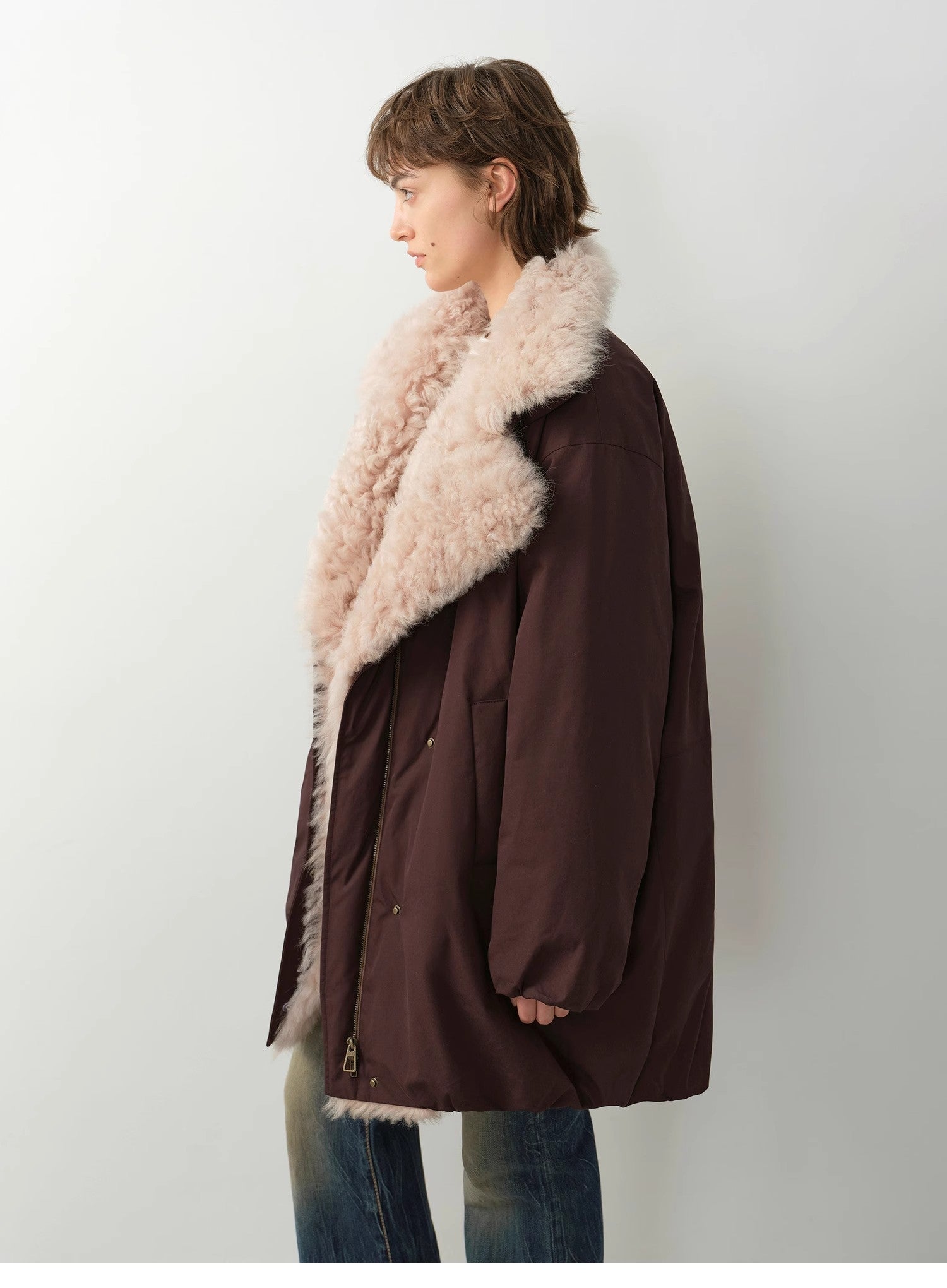 Person wearing a brown coat with beige fur collar against a white background