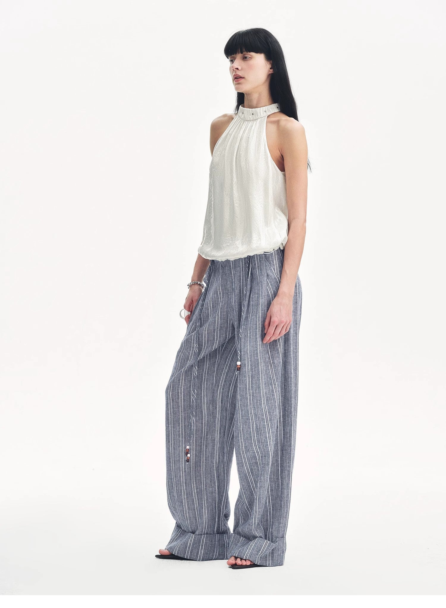 Woman wearing a white sleeveless top and blue striped pants on a white background