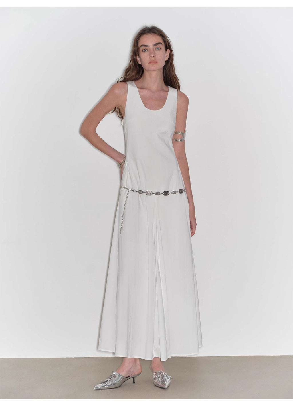Woman wearing a white sleeveless dress with a belt on a plain background
