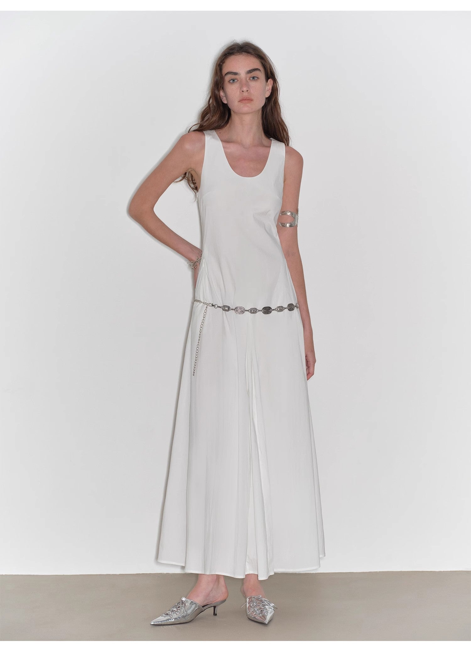 Woman wearing a white sleeveless dress with a belt on a plain background